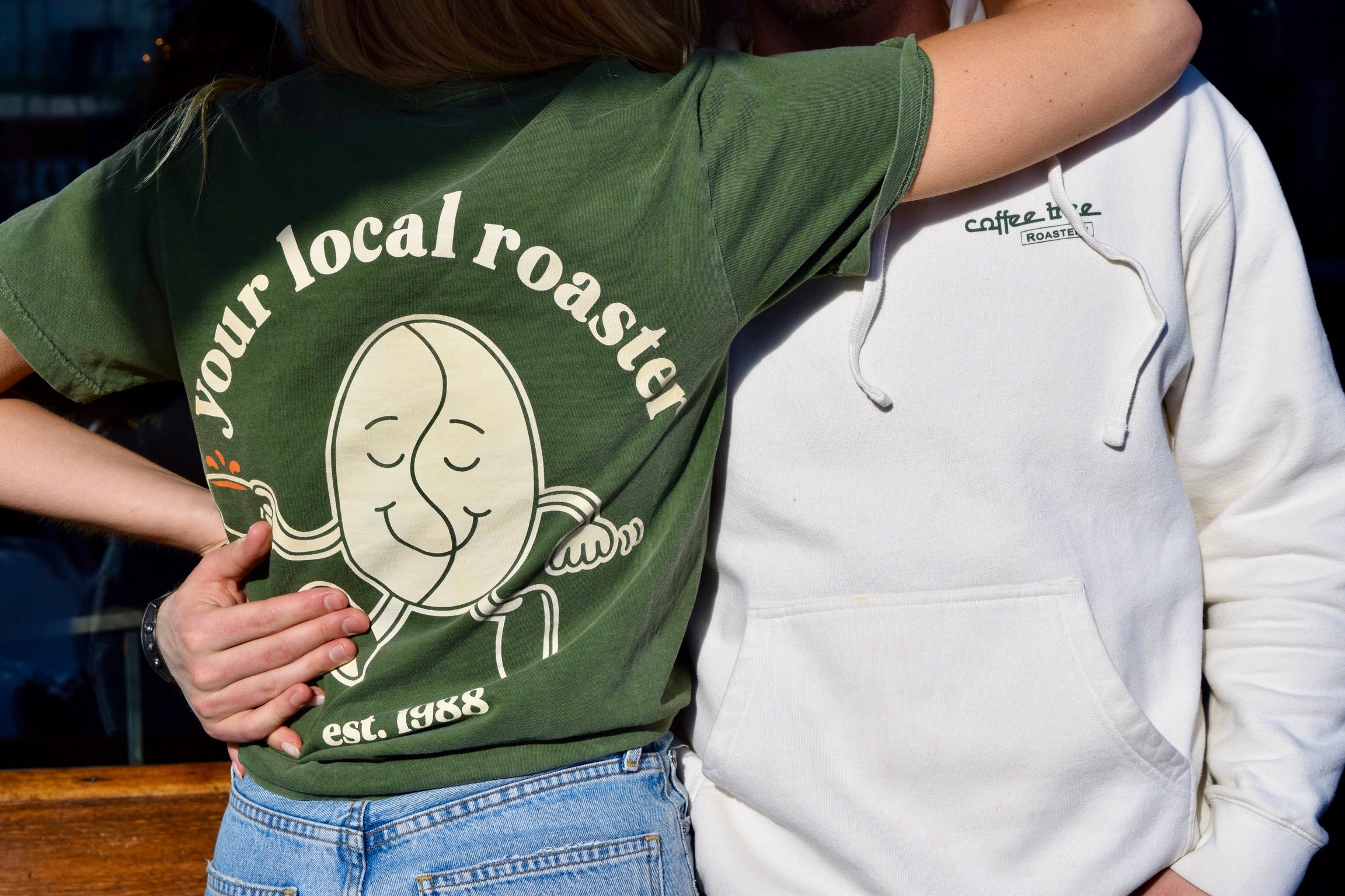 Three people wearing your local roaster sweaters and t-shirts