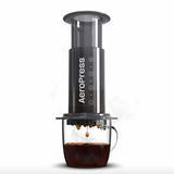 AeroPress coffee maker brewing black coffee into a clear glass cup