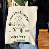 Coffee Tree Roastery tote bag being carried outdoors in sunlight with “your local roaster” design