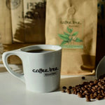 Coffee Tree Roastery mug filled with coffee beside roasted beans and coffee bag in warm natural light